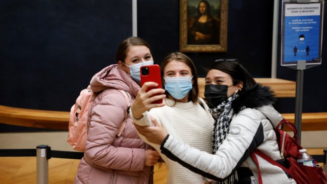 De máscara, visitantes fazem selfie com o quadro da Monalisa ao fundo, no Museu do Louvre, em Paris.